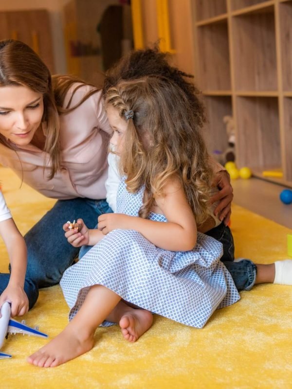 tutor-hugging-adorable-kids-on-carpet-in-kindergarten-1.jpg